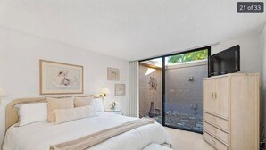 A bedroom with a large bed, a wardrobe, a television, and a sliding glass door leading to an outdoor area.