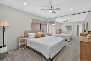 Een moderne slaapkamer met een groot bed, een plafondventilator en een spiegel die de kamer weerspiegelt.