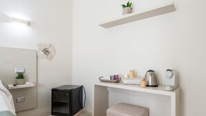 A modern bedroom with a bed, bedside table, and a small desk with a kettle, cup, and plant. - Il Ginepro - Suite Cactus (Pula)