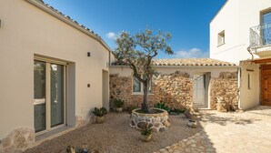 A courtyard with a stone wall, a tree, and potted plants. - Il Ginepro - Suite Cactus (Pula)