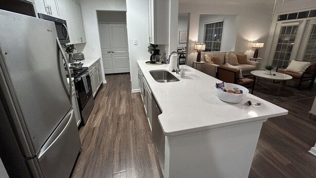 Una cocina moderna con refrigerador, estufa y lavamanos integrados. Cuenta con un comedor con mesa y sillas, y una sala de estar con sofá y lámpara.