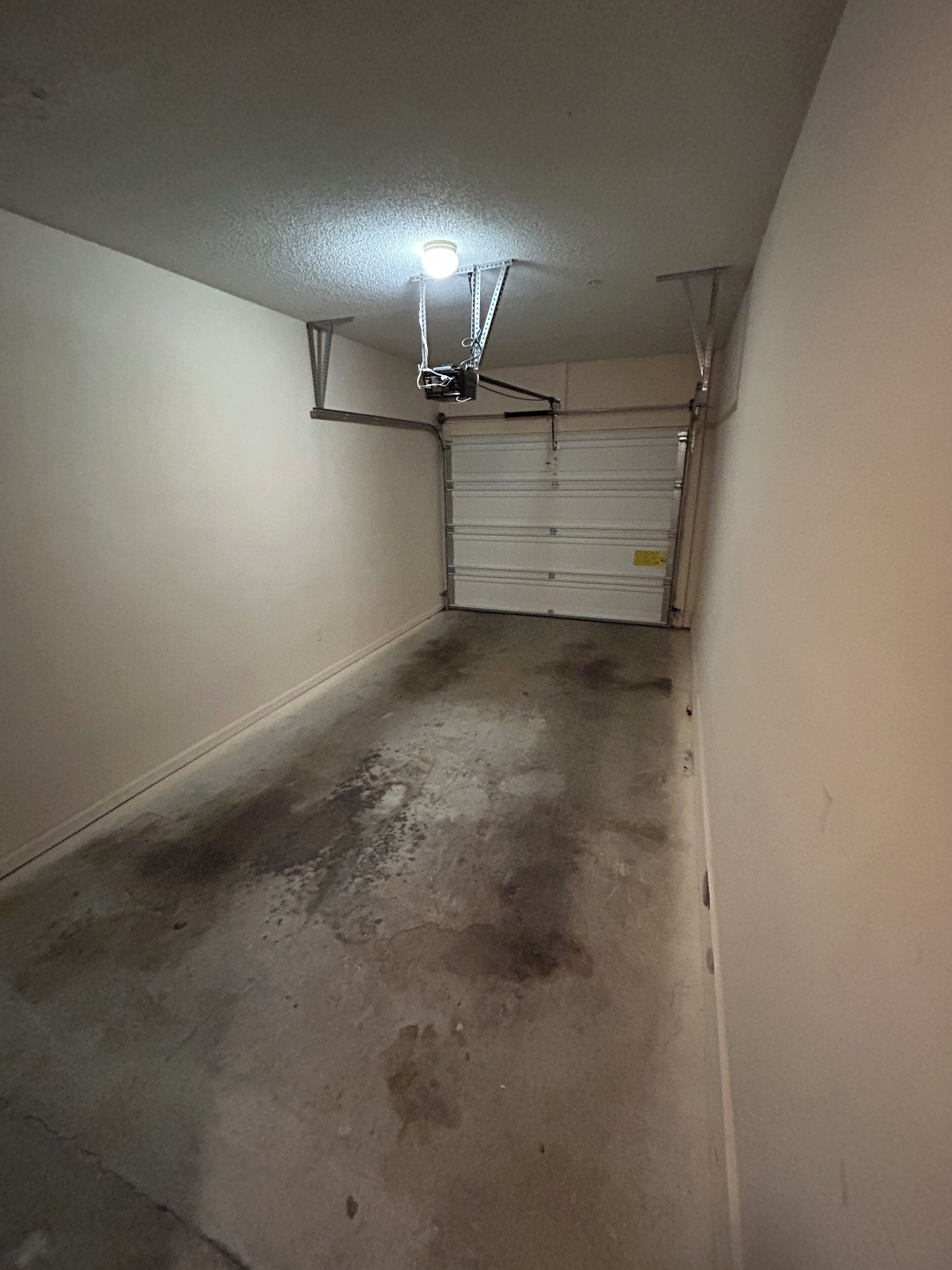 Een garage met een betonnen vloer, een gesloten garagepoort en een plafondlamp.