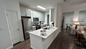 Una cocina moderna con armarios blancos, un refrigerador de acero inoxidable, un microondas y una isla grande con un bol.