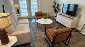 Una sala de estar moderna con sofá, sillones, una mesa de centro, televisor y una lámpara.
