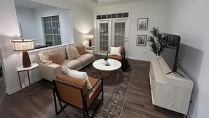 Una sala de estar con sofá, mesa de centro y sillas, un ventilador de techo y un televisor sobre un mueble.