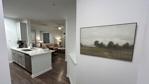 Una cocina moderna con una isla central, una zona de comedor con sofá y mesa, y una sala de estar con sofá y lámpara.