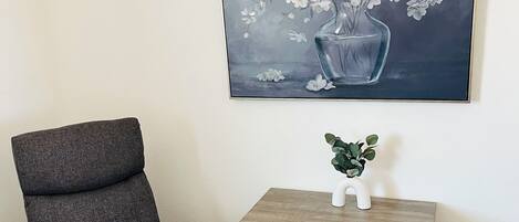 Un sillón gris y una mesita de noche de madera con un jarrón de flores blancas.