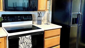 A kitchen with wooden cabinets, a black refrigerator, a black stove, and a microwave. - Kid & Pet Friendly Farm Guesthouse (Golden Valley)