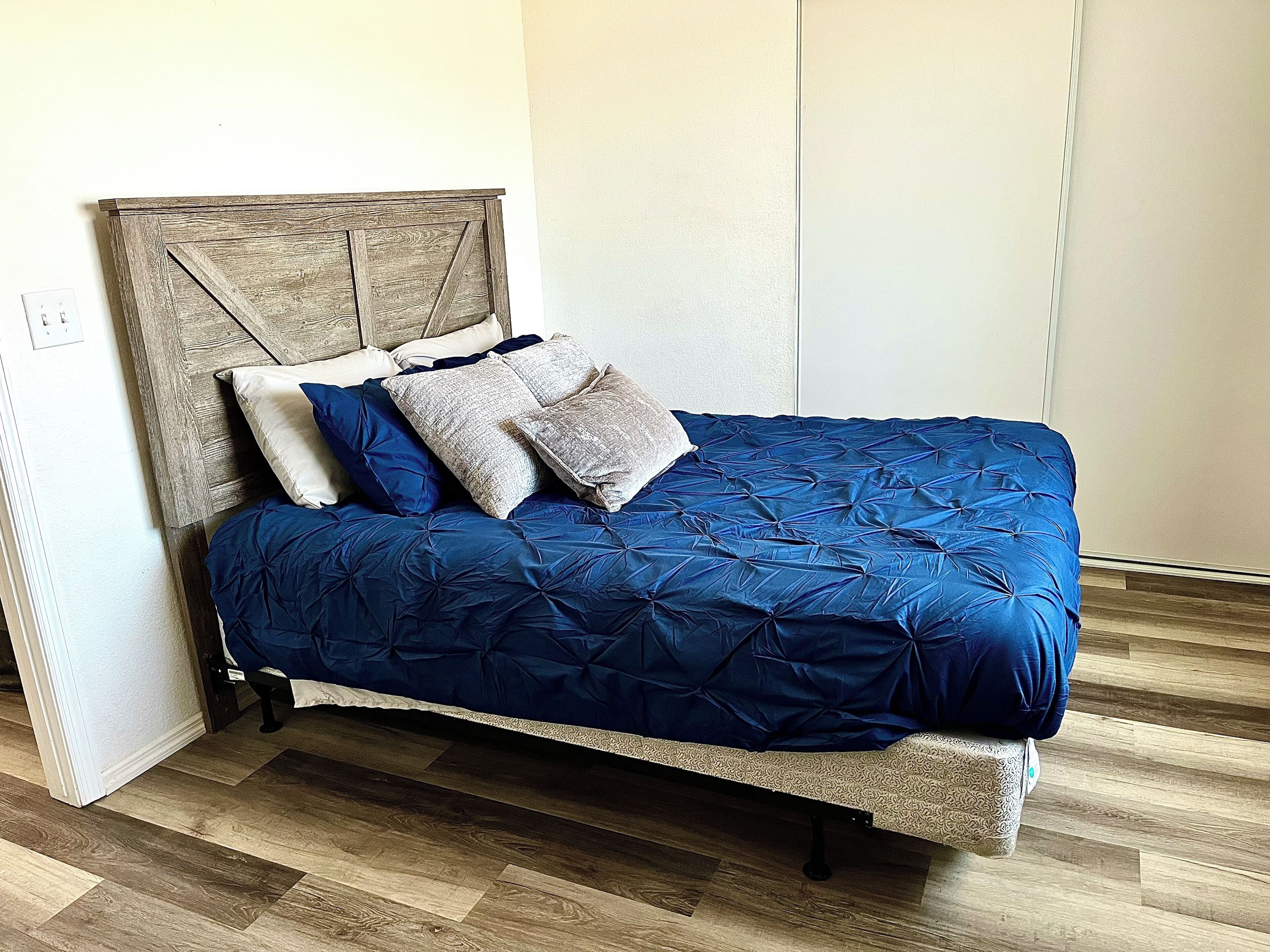 Un lit avec une tête de lit en bois, une couvre-lit bleue matelassée et plusieurs oreillers.