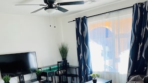 A modern living room with a sofa, a TV, a ceiling fan, a dining table with chairs, and a potted plant. - Kid & Pet Friendly Farm Guesthouse (Golden Valley)