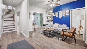 Un salon avec un escalier, un ventilateur de plafond, un mur d’accent bleu et une bibliothèque.