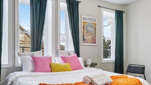 Une chambre d’hôtel avec un lit, des oreillers, une couverture, une chaise et une fenêtre avec des rideaux.
