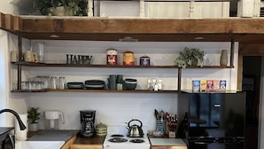 Una cocina con estufa, lavamanos y repisas superiores que contienen utensilios de cocina y un letrero que dice 'HAPPY'.