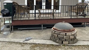 Un edificio con un amplio ventanal corredera, una terraza con mobiliario exterior y un pozo de fuego de piedra.