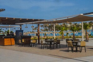 Relax and socialize in our shaded outdoor seating area, featuring comfortable tables and chairs beneath a vibrant mural.