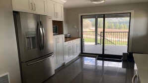 A kitchen with a stainless steel refrigerator, white cabinets, a wooden countertop, and a sliding glass door leading to a balcony with a view of a grassy area and trees. - Silver Oak Luxe Stay | King Bed | Retreat (Arrow Creek)