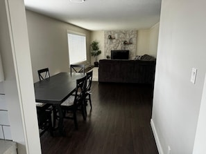 A dining area with a dark wooden table and chairs, a stone accent wall, and a flat-screen TV. - Silver Oak Luxe Stay | King Bed | Retreat (Arrow Creek)