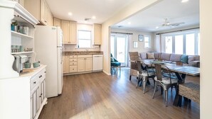 Una cocina amplia con suelo de madera, un comedor con mesa y sillas, y una sala de estar con sofá y ventilador de techo.
