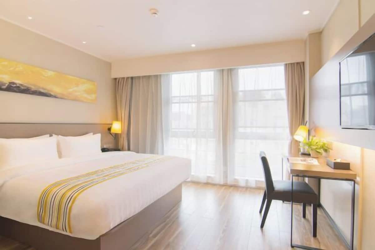 A hotel room with a large bed, a desk, a chair, and a window with curtains.