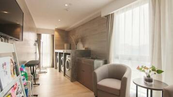 Quarto de hotel moderno com televisão de tela plana, sofá, mesa redonda pequena e vista para a cidade.