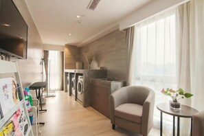 A modern hotel room with a flat-screen TV, a sofa, a small round table, and a view of the city. - Home Inn Select (Shanghai Zhoupu Wanda Plaza Branch) (Shanghai)