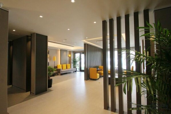A modern hotel lobby with a reception desk, seating area, and a large plant. - Home Inn Select (Shanghai Zhoupu Wanda Plaza Branch) (Shanghai)
