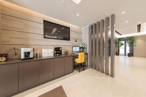 A reception desk with a flat-screen TV, a coffee machine, and a plant. - Home Inn Select (Shanghai Zhoupu Wanda Plaza Branch) (Shanghai)