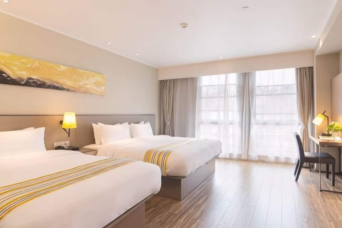 A hotel room with two beds, a desk, a chair, and a large window with curtains.