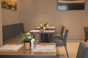 Ένα εστιατόριο με τραπέζια στρωμένα για φαγητό, στο οποίο υπάρχει ένα βάζο με λουλούδια και ένα κερί.