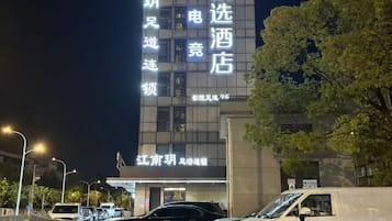 Um hotel com letreiros iluminados, área de estacionamento e uma árvore em primeiro plano.