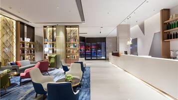 A modern hotel lobby with a seating area, a reception desk, and a bookshelf.