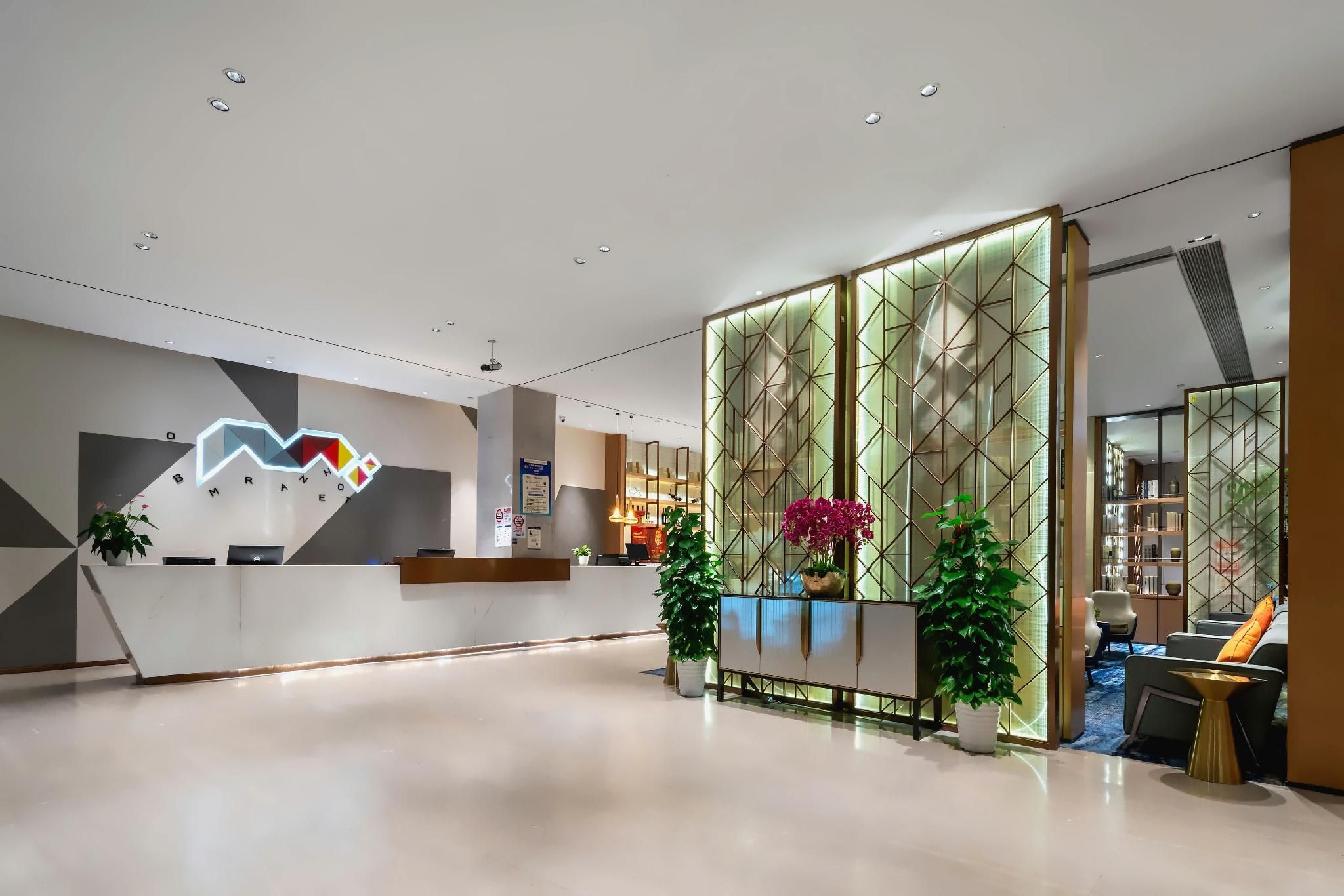 A modern hotel lobby with a reception desk, a geometric wall design, and a seating area with a view of the interior.