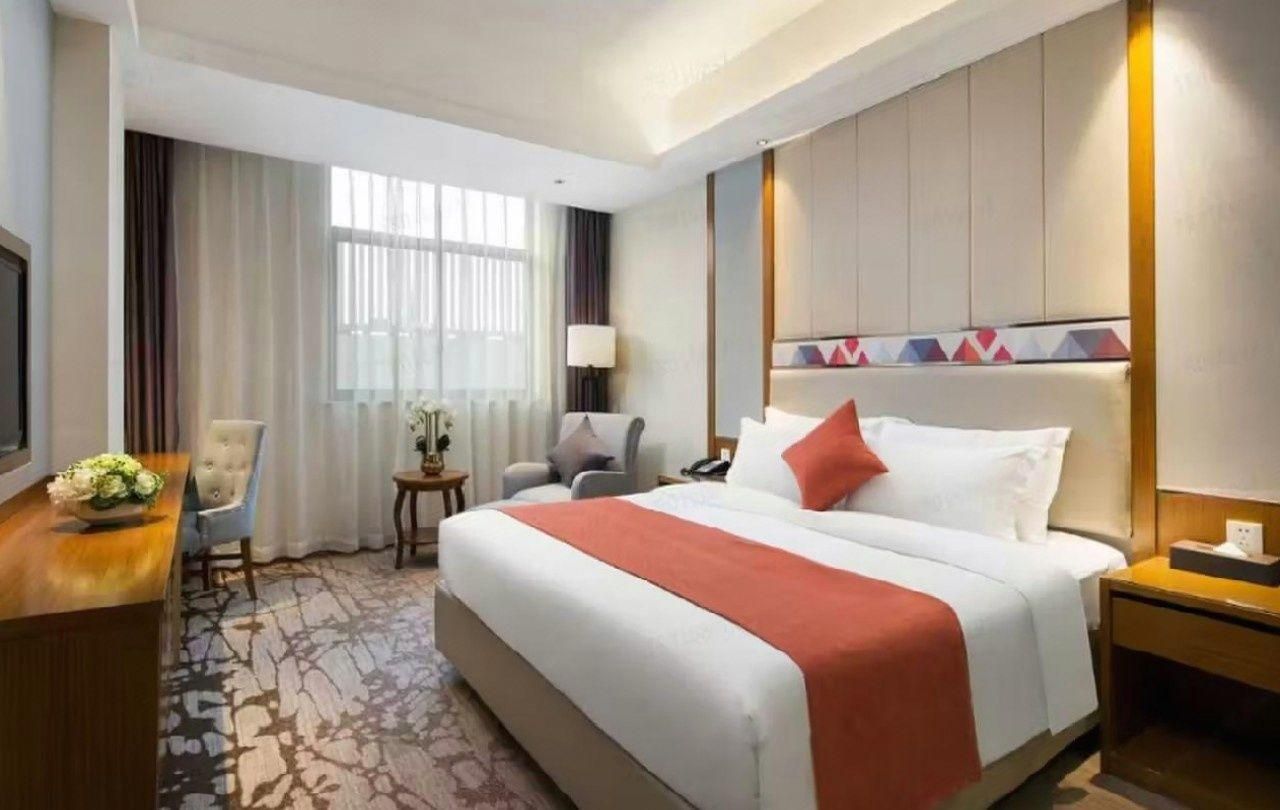 A hotel room with a large bed, a desk, a chair, a lamp, and a window with curtains.