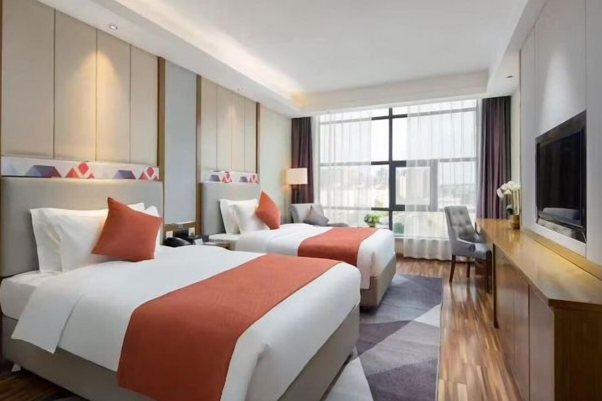 A hotel room with two beds, a TV, a desk, and a large window.