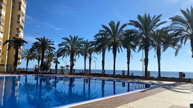 Una piscina con muelle de madera, palmeras y un edificio al fondo.