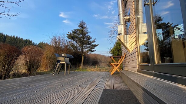 A wooden deck with a metal structure, a chair, and a table. - Tinyhouse in the middle of nature! Perfect for a spontaneous break! (Bad Endbach)