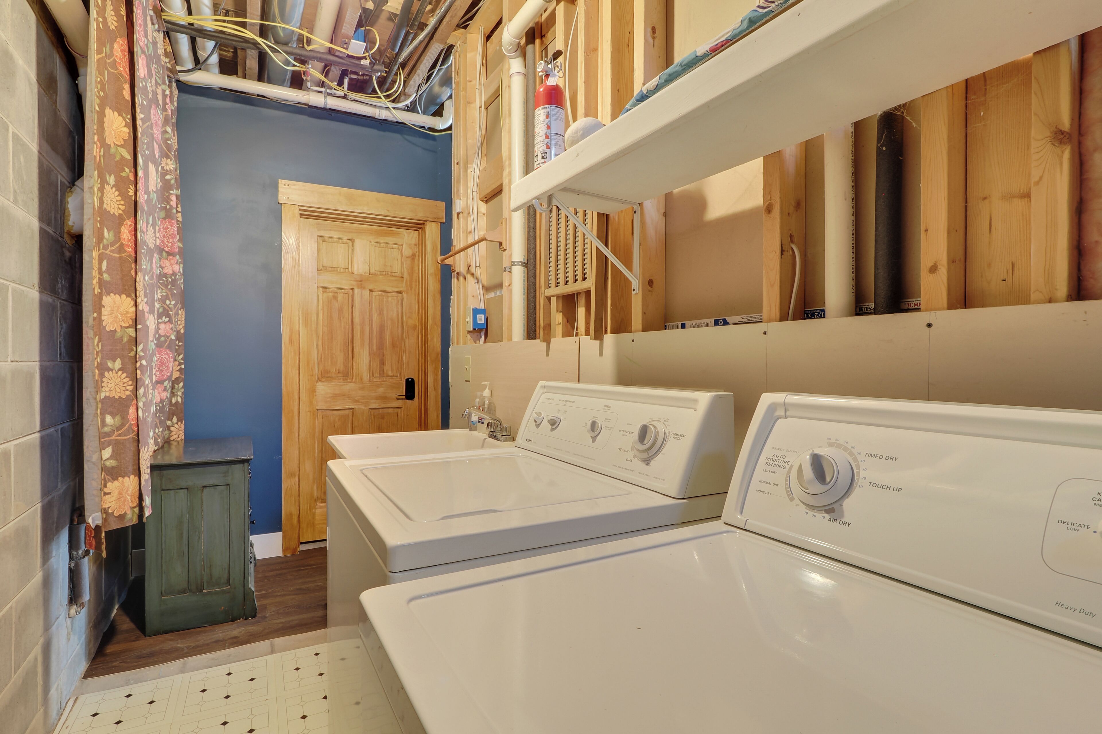 A laundry room with two white front-loading washers, wooden cabinets, and a door leading to another room.