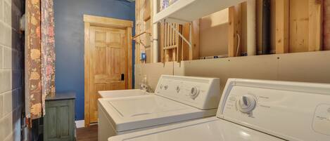 A laundry room with two white front-loading washers, wooden cabinets, and a door leading to another room.