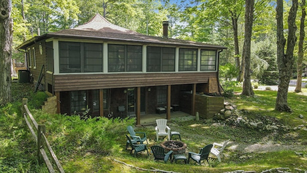 A two-story cabin with large windows, a covered porch, and outdoor seating. - Updated cabin sleeps 8. Pet friendly, and has private neighborhood beach. (Charlevoix)
