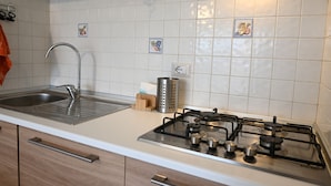 A kitchen with a stainless steel sink, a gas stove, and white tiled walls. - SE140 – Senigallia, two-room apartment on the Mameli seafront (Senigallia)