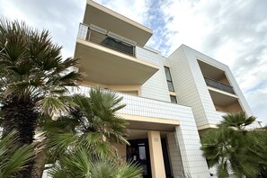 Een meerlaags gebouw met balkons, palmbomen en een heldere lucht.