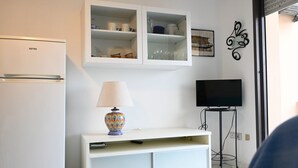 A living room with a white cabinet, a TV on a stand, a lamp, and a refrigerator. - SE140 – Senigallia, two-room apartment on the Mameli seafront (Senigallia)