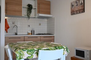 Een keuken met witte kastjes, een wit aanrecht, een kookplaat, een spoelbak en een magnetron.
