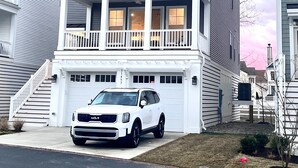 Una casa de dos pisos con balcón y cochera, con un SUV blanco estacionado al frente.