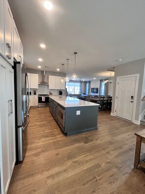 A modern kitchen with stainless steel appliances, a central island, pendant lighting, and a dining area with a view.