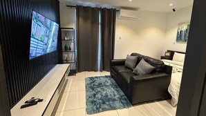 A modern living room with a flat-screen TV, a black leather sofa, a blue rug, and a white console table. - EBS LEGEND ONE BEDROOM DUPLUX embassy (Accra)
