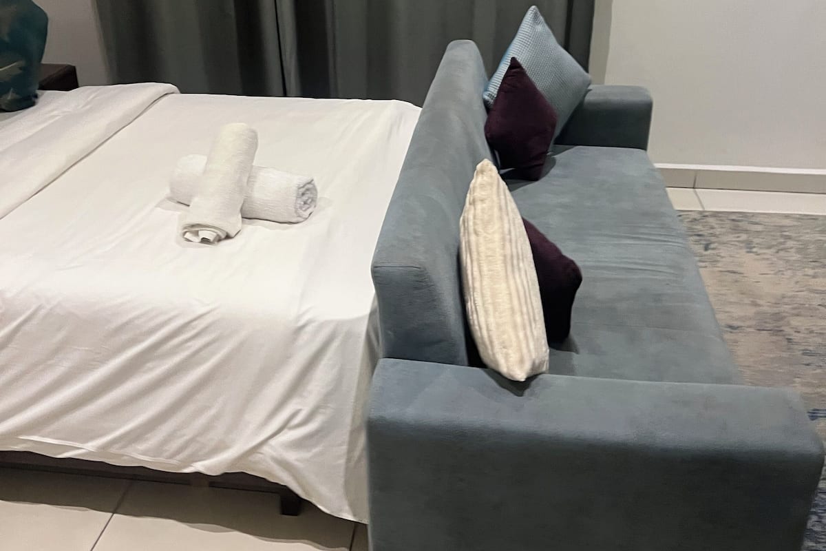 A room with a bed, a grey sofa, and a patterned rug.