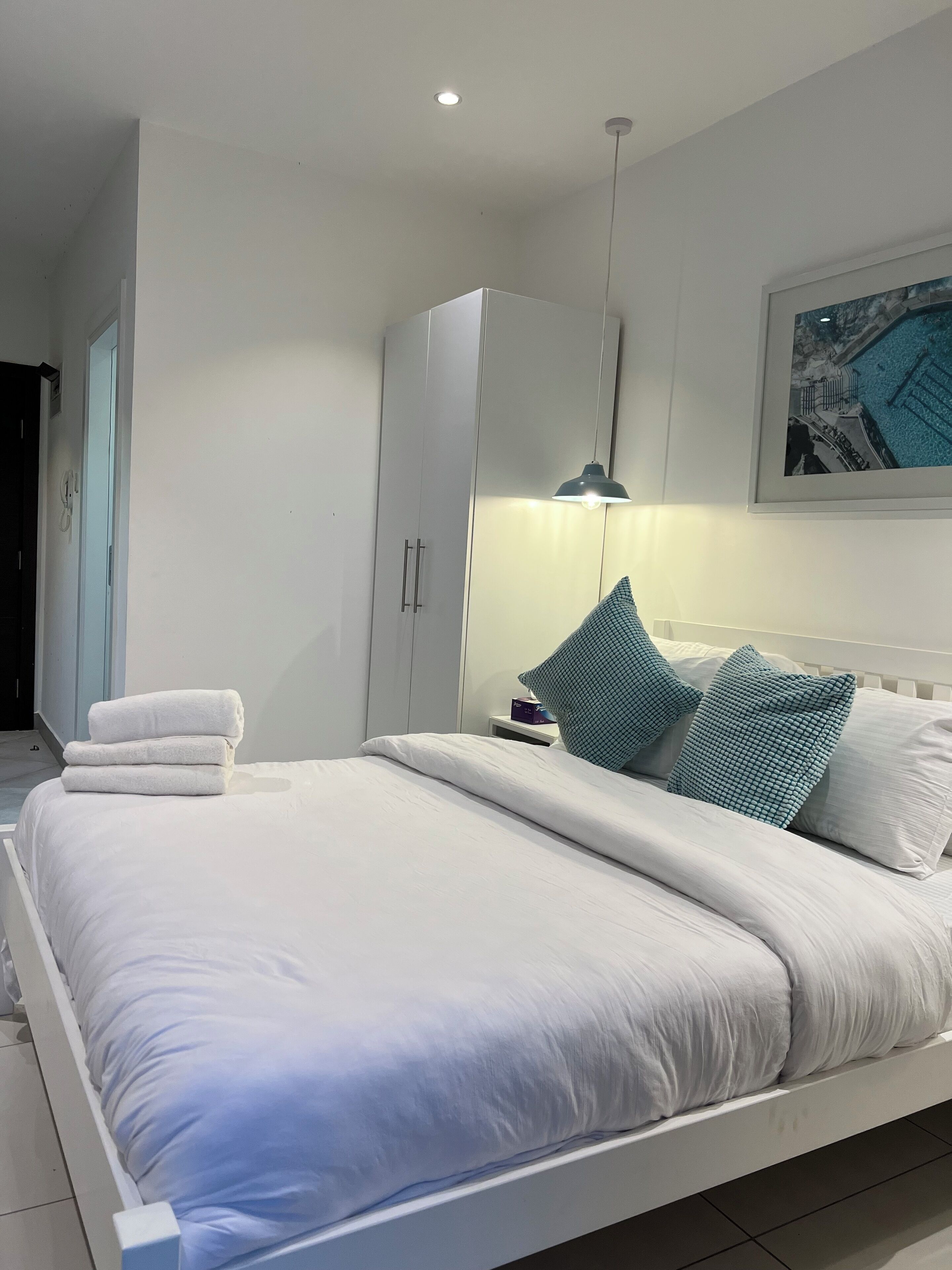 A modern bedroom with a large bed, white wardrobe, and a framed picture on the wall.