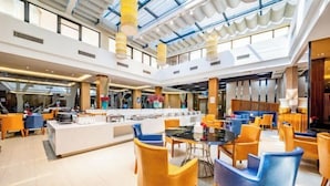 Een ruime hotel lobby met een hoge plafond, moderne zithoeken en een centrale bar.