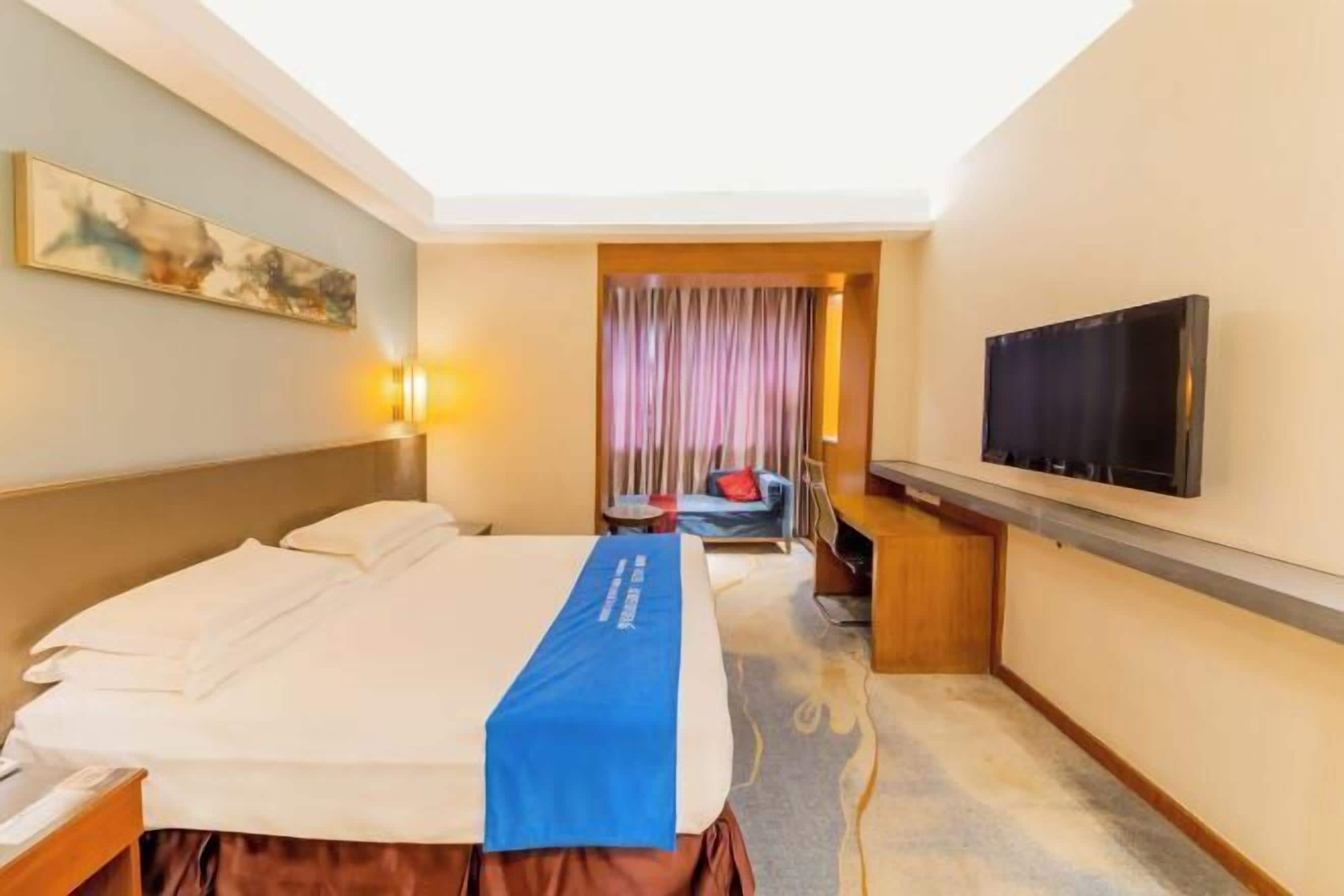 A hotel room with a bed, a desk, a chair, a television, and a painting on the wall.